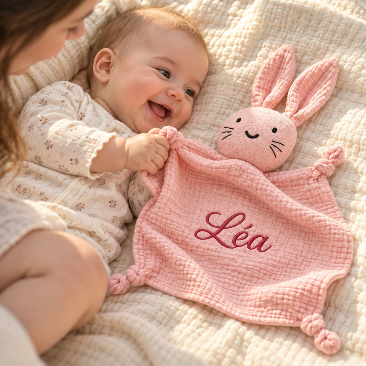 Un bébé éveillé et souriant attrape son doudou lapin brodé Léa