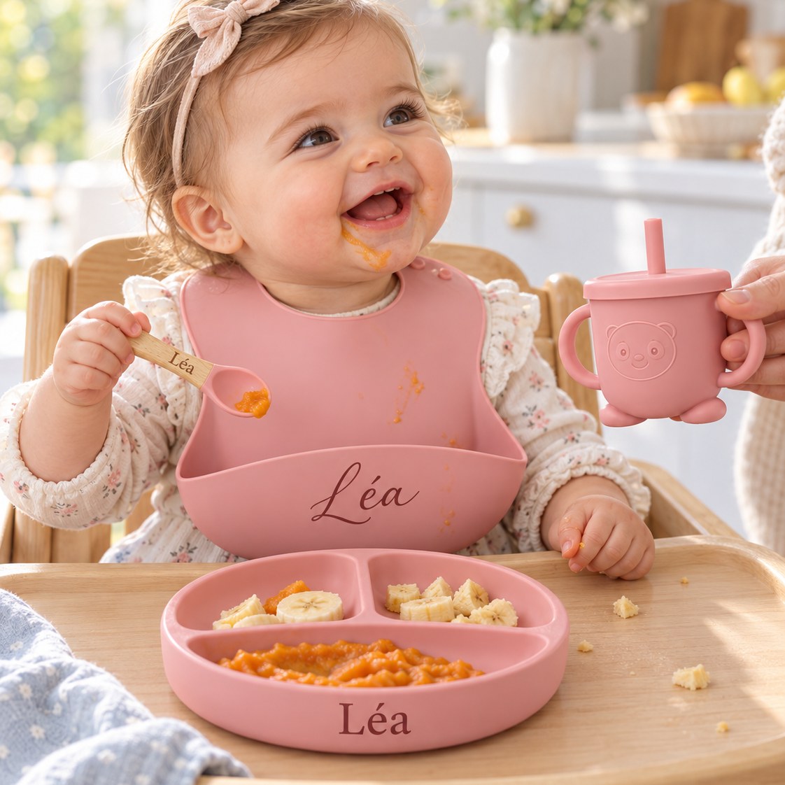 Bébé qui mange avec son set repas rose personnalisé au prénom Léa : bavoir, assiette à compartiments et gobelet